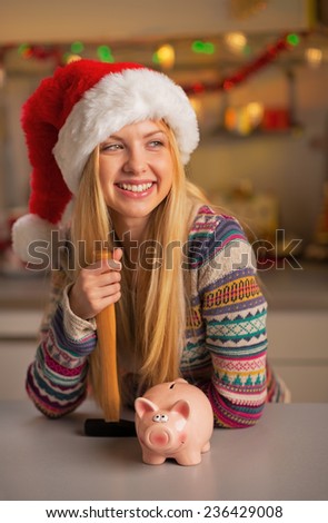 Portrait of smiling teenager girl in santa hat with piggy bank and hammer