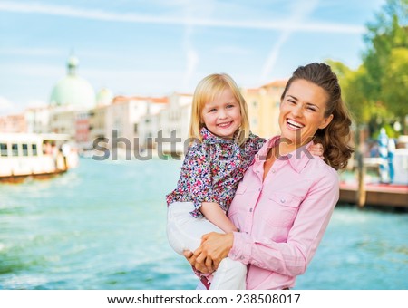 Portrait of happy mother and baby standing on grand canal embankment in venice, italy