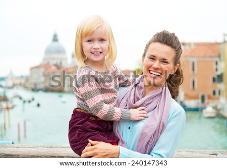 Portrait of smiling mother and baby girl standing on bridge with grand canal view in venice, italy