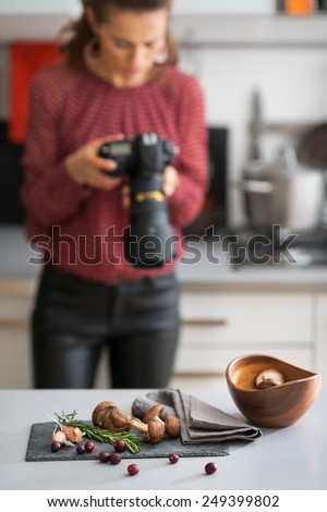 Closeup on mushrooms lingonberries and rosmarinus on table and female food photographer in background