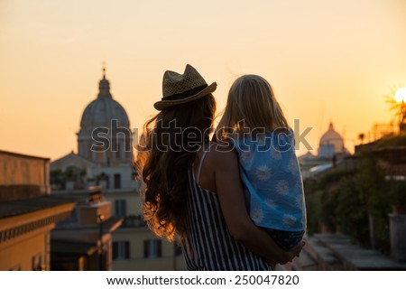 Silhouette of mother and baby girl looking on rooftops of rome on sunset. rear view