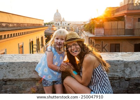 Portrait of happy mother and baby girl on street overlooking rooftops of rome on sunset