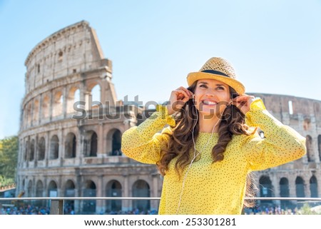 Portrait of happy young woman with audio guide in front of colosseum in rome, italy