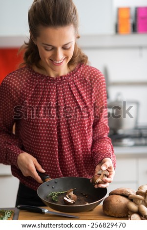 Happy young housewife cooking mushrooms