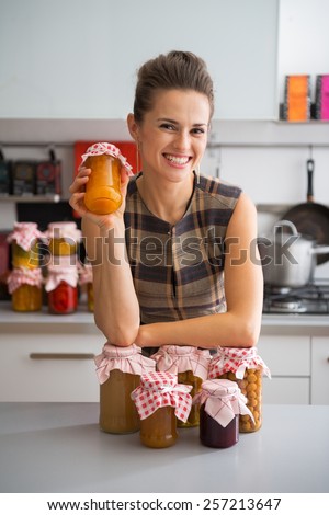 Portrait of happy young housewife among jars with homemade fruits jam and pickled vegetables
