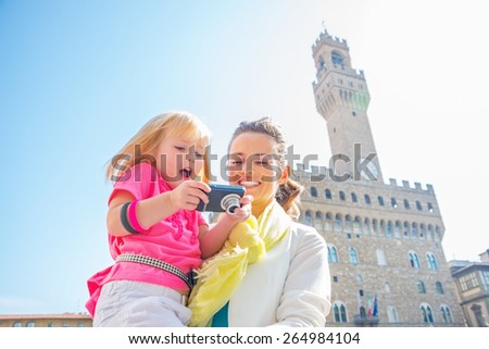 Happy mother and baby girl checking photos in camera in front of palazzo vecchio in florence, italy in florence, italy