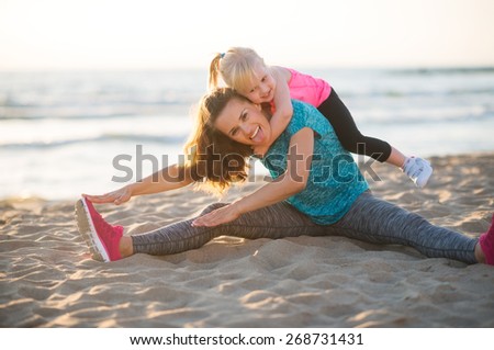 Healthy mother and baby girl stretching on beach in the evening