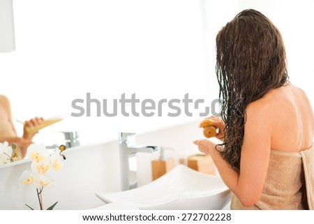 Closeup on young woman applying hair mask in bathroom