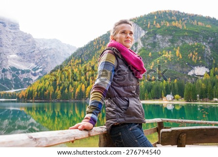 A pensive brunette hiker at Lake Bries wearing outdoor gear is leaning with her hands up against a wooden railing, smiling gently.