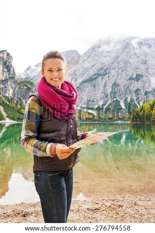 Looking up from her map, a smiling brunette wearing outdoor gear is holding a map while standing on the shores of Lake Bries.
