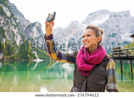 A smiling brunette wearing outdoor gear is taking a photo of the scenery on her digital camera. In the background, the Italian Dolomites are above the lake.