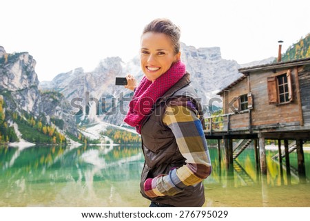A smiling brunette in outdoor gear is aiming her digital camera out at Lake Bries and the Italian Dolomites in the background.