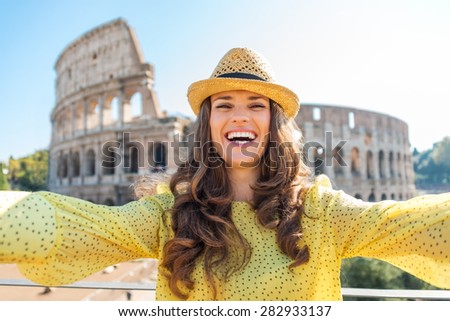 A happy, smiling woman tourist in the summer takes a selfie with the Colosseum in the distance.