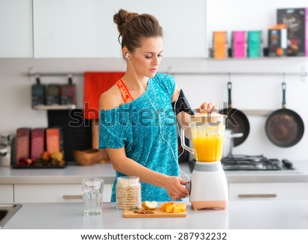 A sporty woman is standing in her kitchen, making a smoothie with fresh, seasonal fruits, nuts, and oats, to complete her healthy start to the morning.