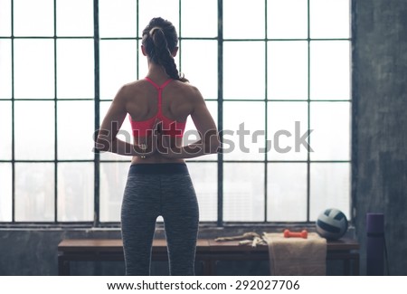 A fit, muscular woman\'s hands clasped behind her back as she is doing the pose in yoga called the tadasana paschima namaskar pose.
