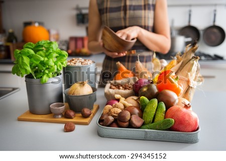 A tray full of Autumn fruits, nuts, and vegetables sits on a kitchen counter. Next to the tray, a wooden cutting board featuring a fresh basil plant and onion promise a delicious meal ahead.