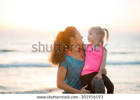 Come here and give me a little kiss. A mother lovingly leans in to her young daughter. The mother is kneeling next to her daughter and holding her close. The sun is going down on another lovely day.
