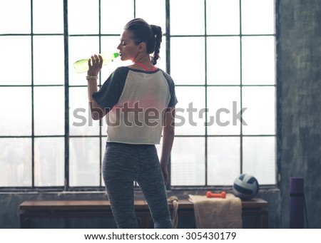 Fit woman in workout gear in profile drinking from water bottle in a loft gym in the city.