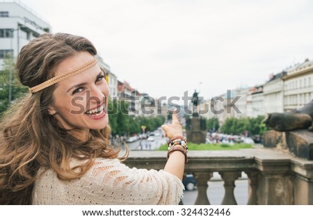 Joyful brunette hippy-looking woman tourist pointing on Saint Wenceslas statue in Prague. Tourism travel concept.