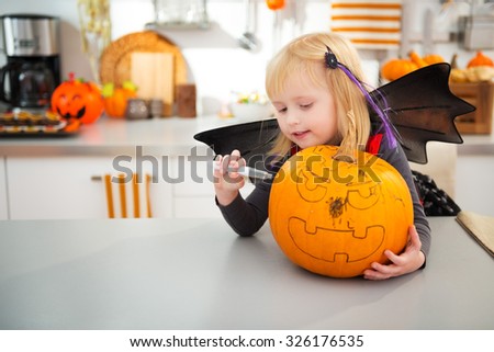 Smiling halloween dressed girl creating big orange pumpkin Jack-O-Lantern in decorated kitchen. Traditional autumn holiday