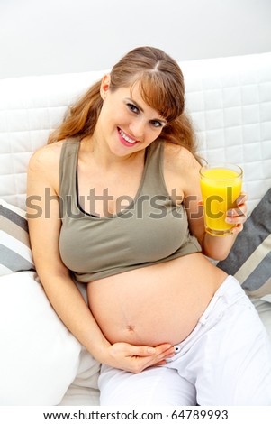 Beautiful pregnant woman sitting on sofa with glass of juice