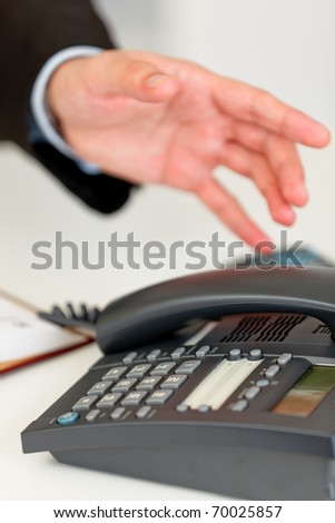 Close up of hand extending to office grey telephone