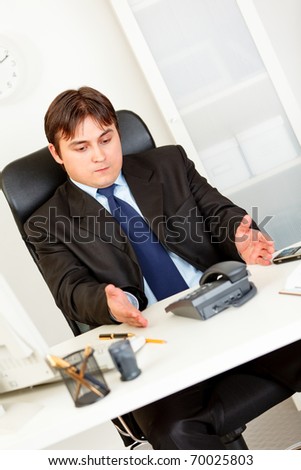 Displeased business man sitting at office desk and waiting important phone call