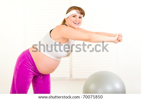 Smiling beautiful pregnant woman making gymnastics  at living room