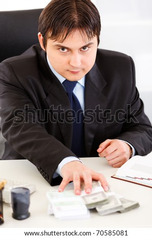Concentrated business man  sitting at office desk and giving money packs