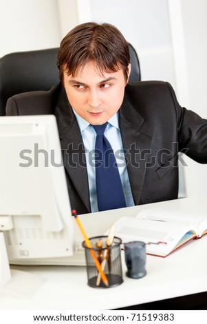 Alert modern business man sitting at office desk  and looking in corner