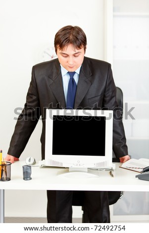 Modern business man standing at office desk and looking in monitors blank screen