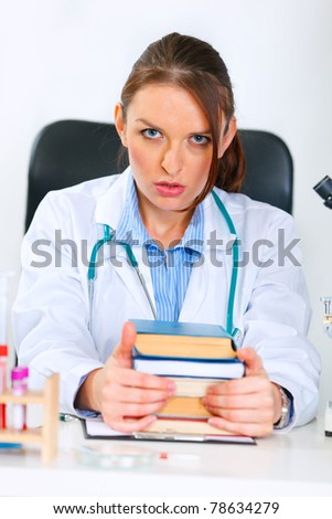 Shocked medical doctor woman sitting at office table with pile of books