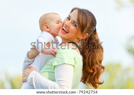 Laughing young mother hugging her baby in hands outdoors
