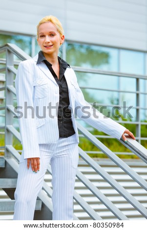 Smiling modern business woman standing on stairs at office building  and holding hand on railing