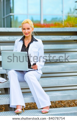 Happy modern business woman sitting on stairs at office building and working on laptop