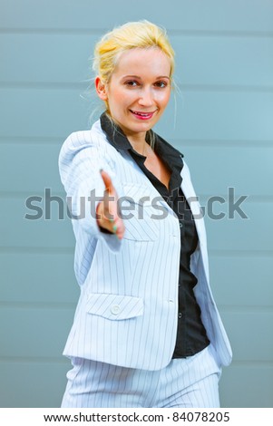 Standing at office building smiling modern business woman stretches out hand for handshake