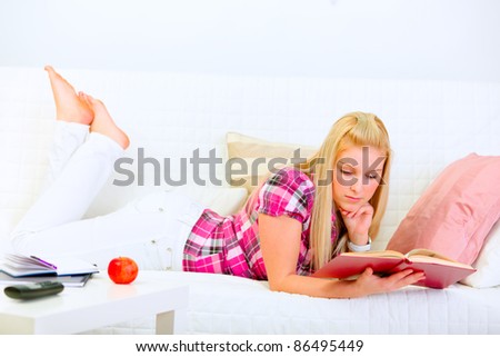 Modern pretty housewife laying on couch and reading book