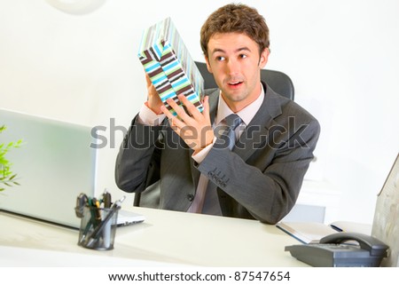 Interested modern businessman shaking present box trying to guess what\'s inside