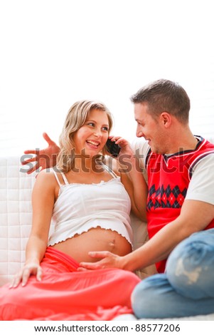 Young pregnant woman sitting with husband on couch and speaking phone