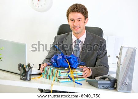 Happy businessman sitting with gift at office desk