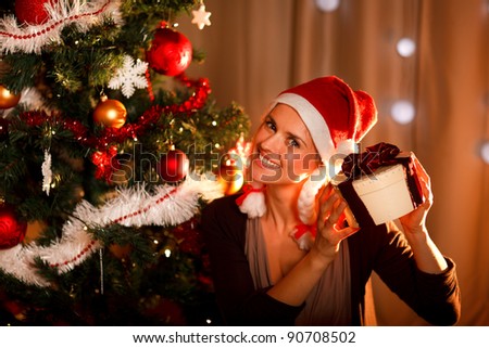 Interested woman near Christmas tree shaking present box trying to guess what\'s inside