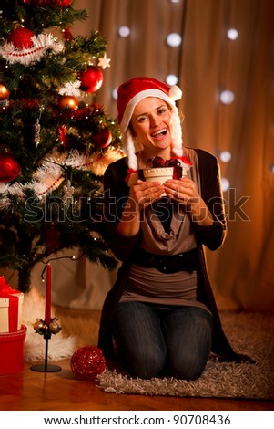 Happy young woman near Christmas tree hugging present box