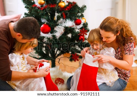Mom and dad looking with twins daughters inside of Christmas socks near Christmas tree