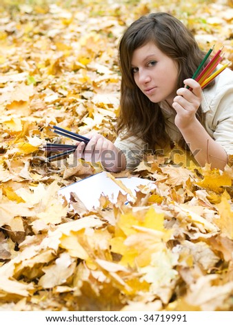girl lying on autumn leaves with pen?ils of different colors like asking what to choose