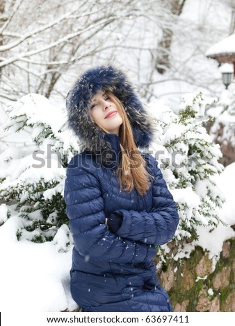 smiling young woman in blue coat outdoors in snow garden