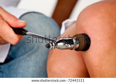 Isolated hand of neurologist testing knee reflex on a female patient using a hammer