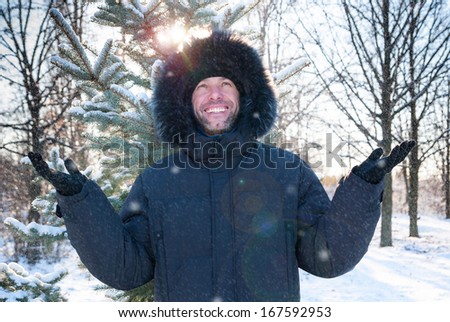 Smiling man wearing fur hooded parka coat in the winter park