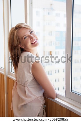 Young smiling woman standing at  window in the new apartment