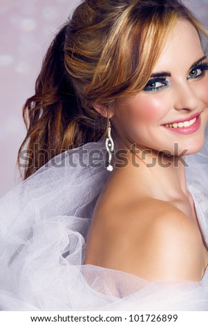 happy beautiful bride with long blond hair in ponytail waring artistic smoky eyeshadow and smiling on bokeh background.