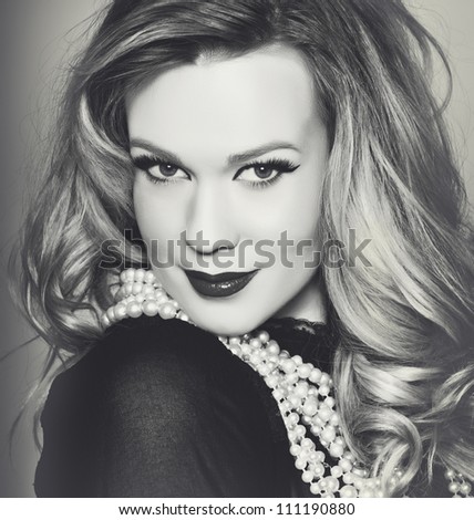 portrait of a beautiful young woman with curly blond hair and glamour make-up wearing a black blouse and pearls in black and white